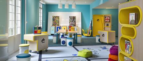 Un cuarto de juegos infantil, lleno de juguetes educativos, cuenta con un amplio ventanal y una alfombra con motivos de sol.
