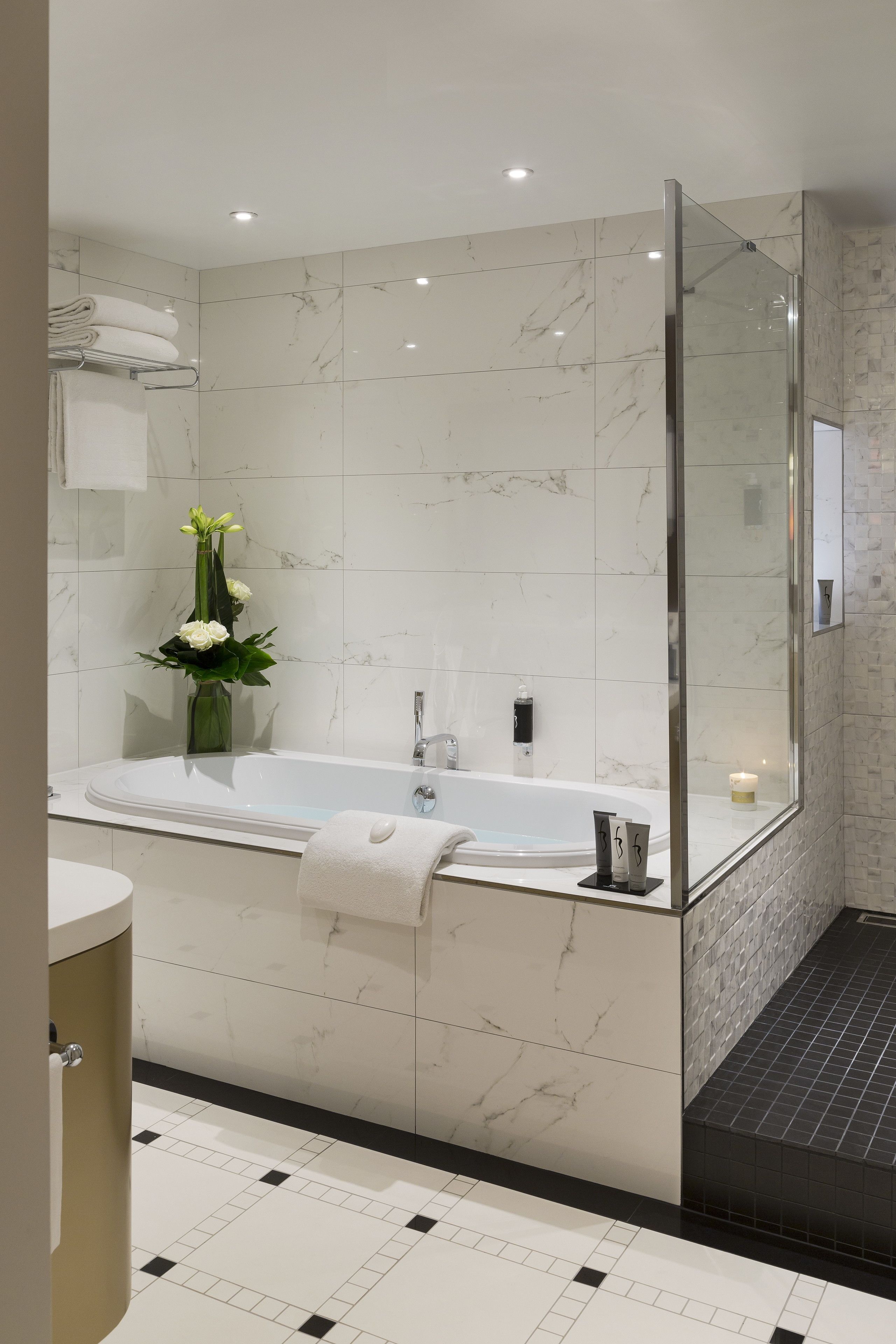 A modern bathroom with a large bathtub, a glass shower enclosure, and a marble-tiled wall.