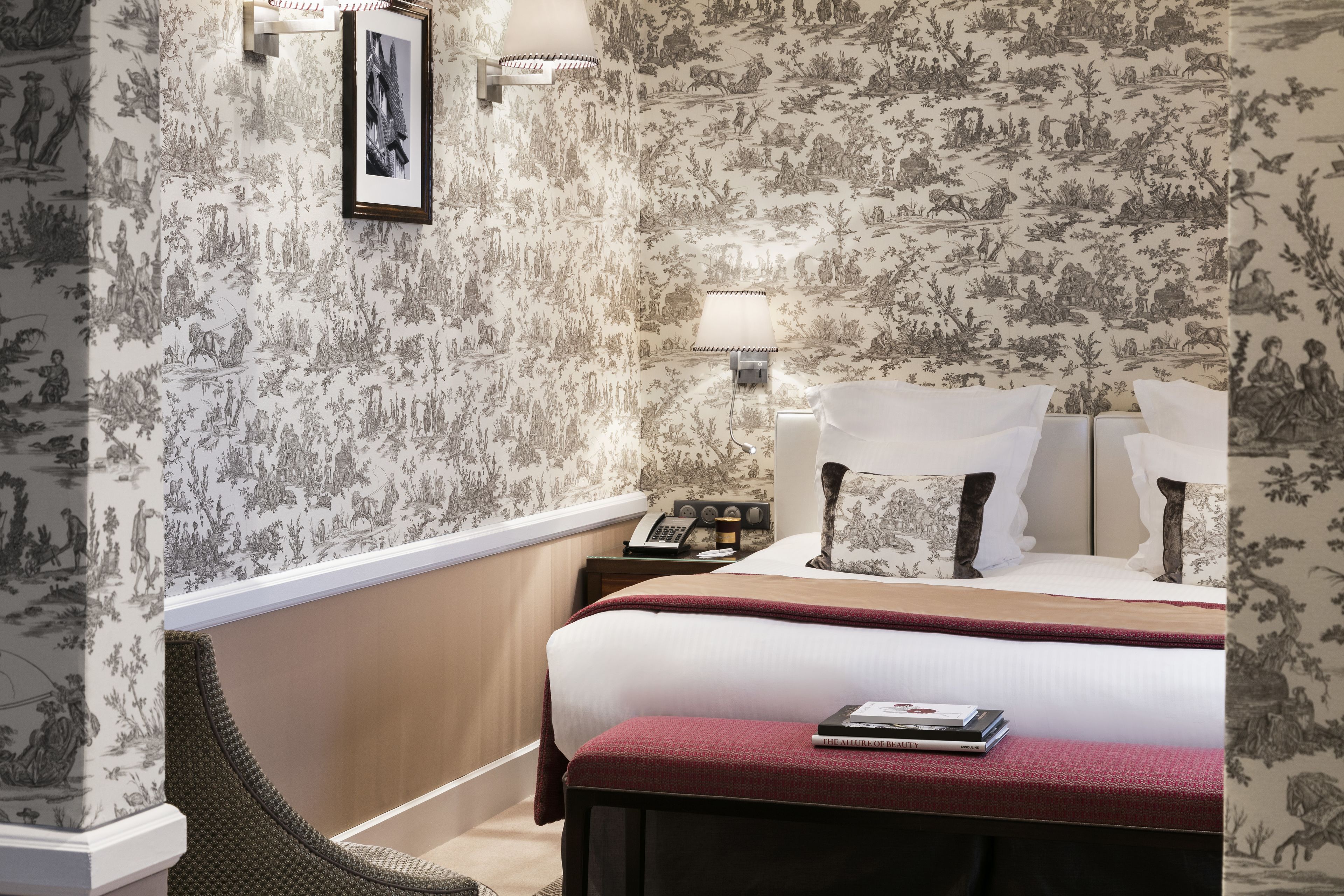A hotel room with a large bed, a bedside table with a lamp, a telephone, and a framed picture on the wall.