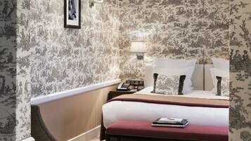 A hotel room with a large bed, a bedside table with a lamp, a telephone, and a framed picture on the wall.