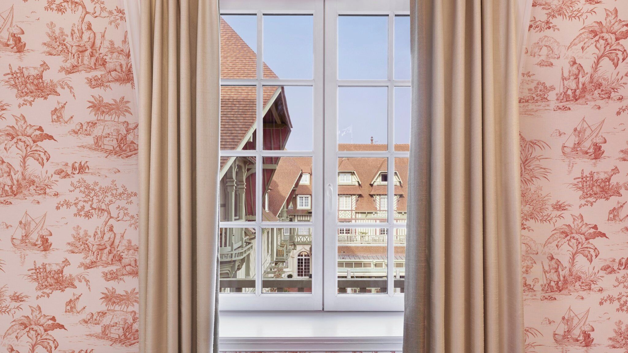 A room with a large window, beige curtains, and a view of traditional European architecture.