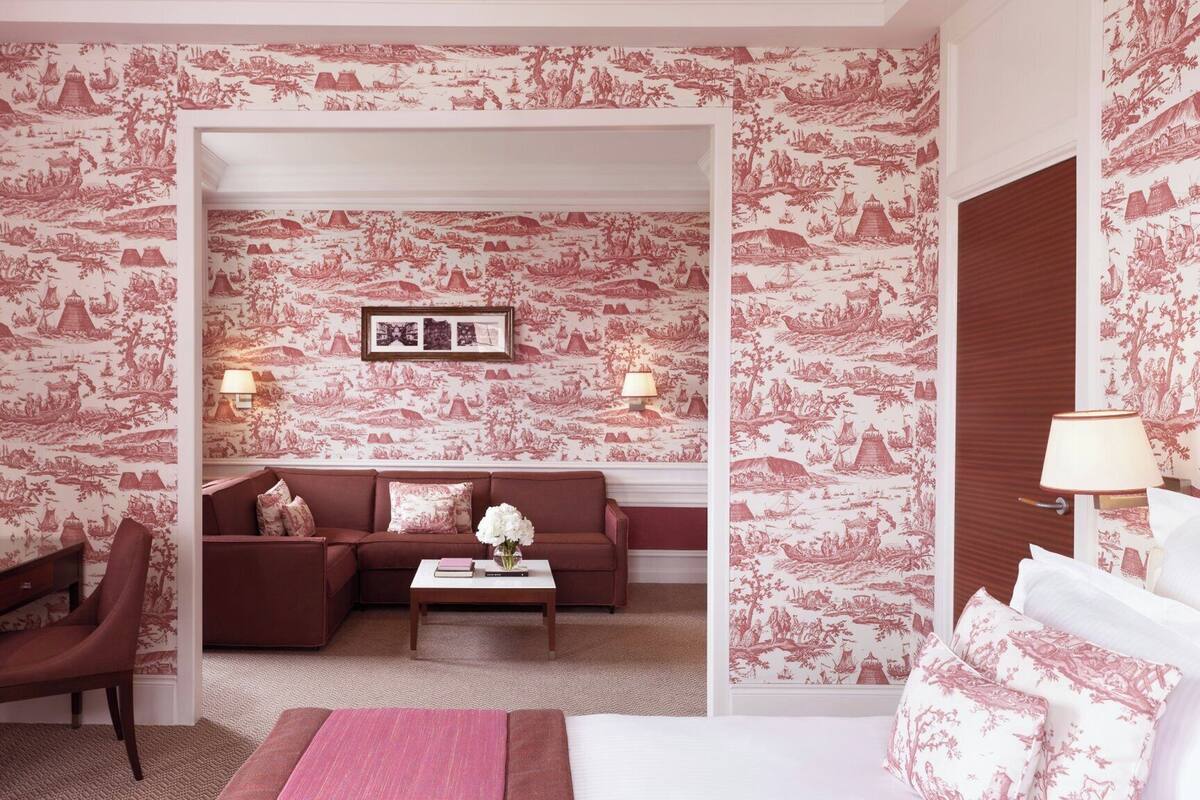 A room with a large bed, a sofa, a coffee table, and a desk with a chair. There are two wall-mounted lamps and a framed picture above the sofa.