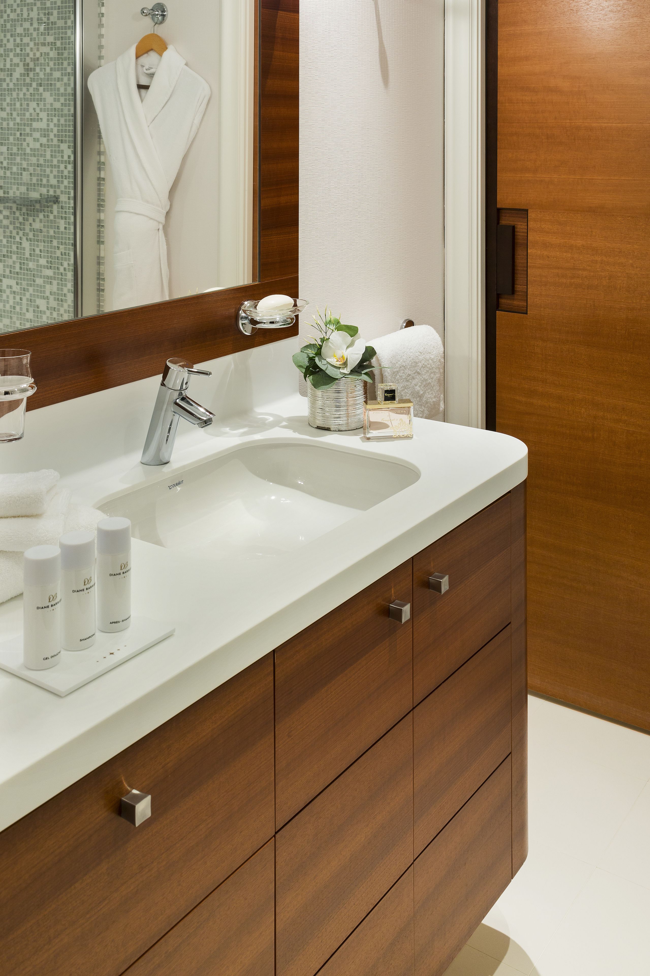 Une salle de bain moderne avec un lavabo blanc, un meuble-lavabo en bois et un miroir qui reflète une robe et une serviette.