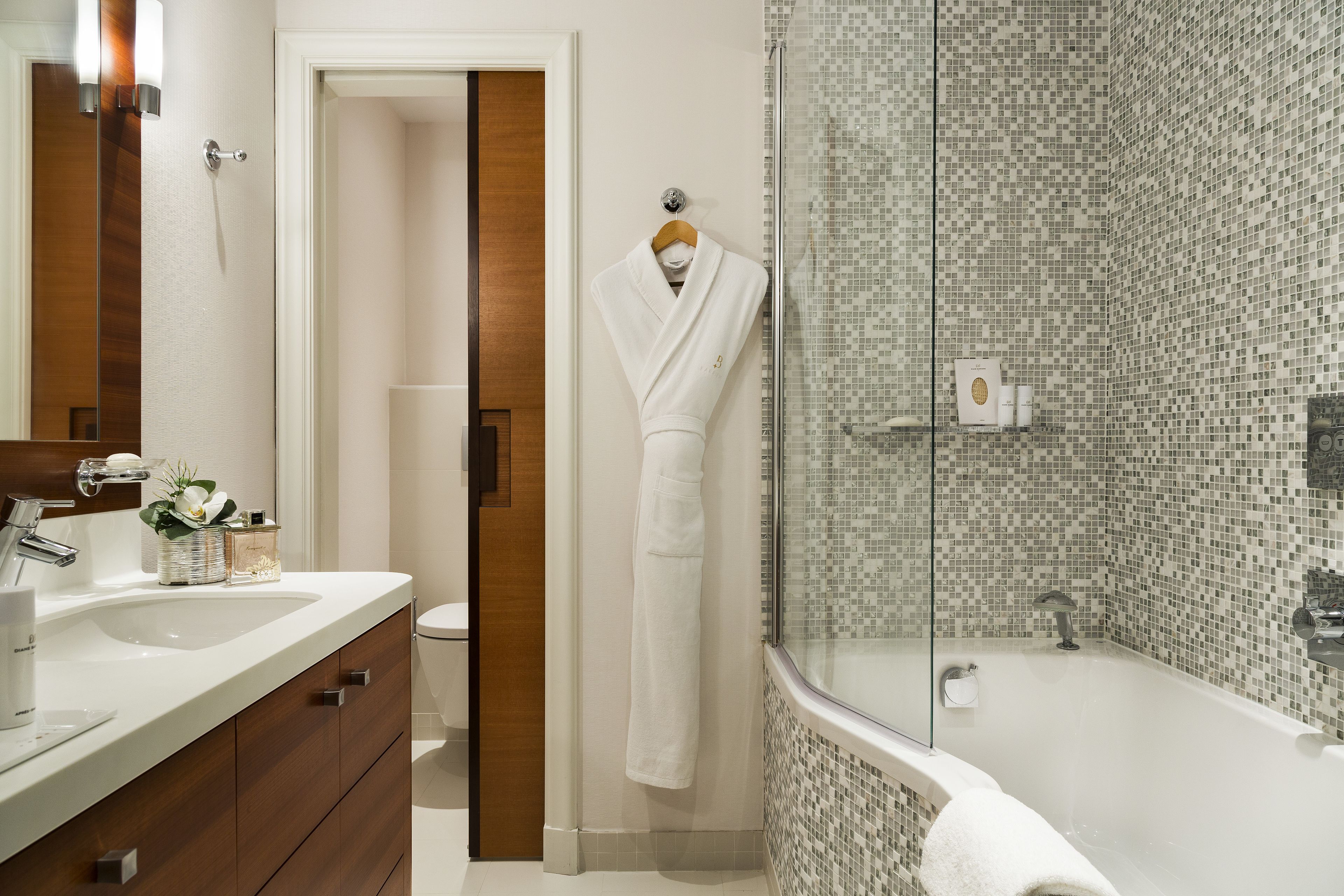 A bathroom with a white sink, wooden vanity, a glass-enclosed shower, and a white robe hanging on a hook.