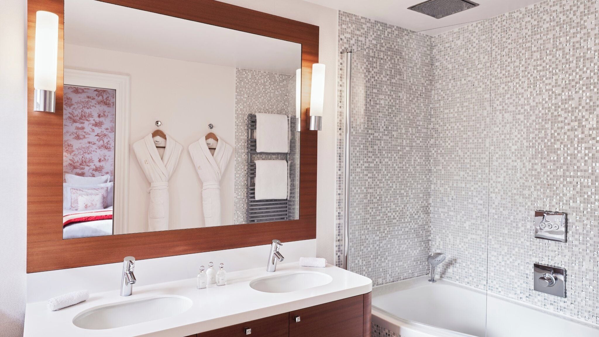 A modern bathroom with two sinks, a large mirror, and a shower area.