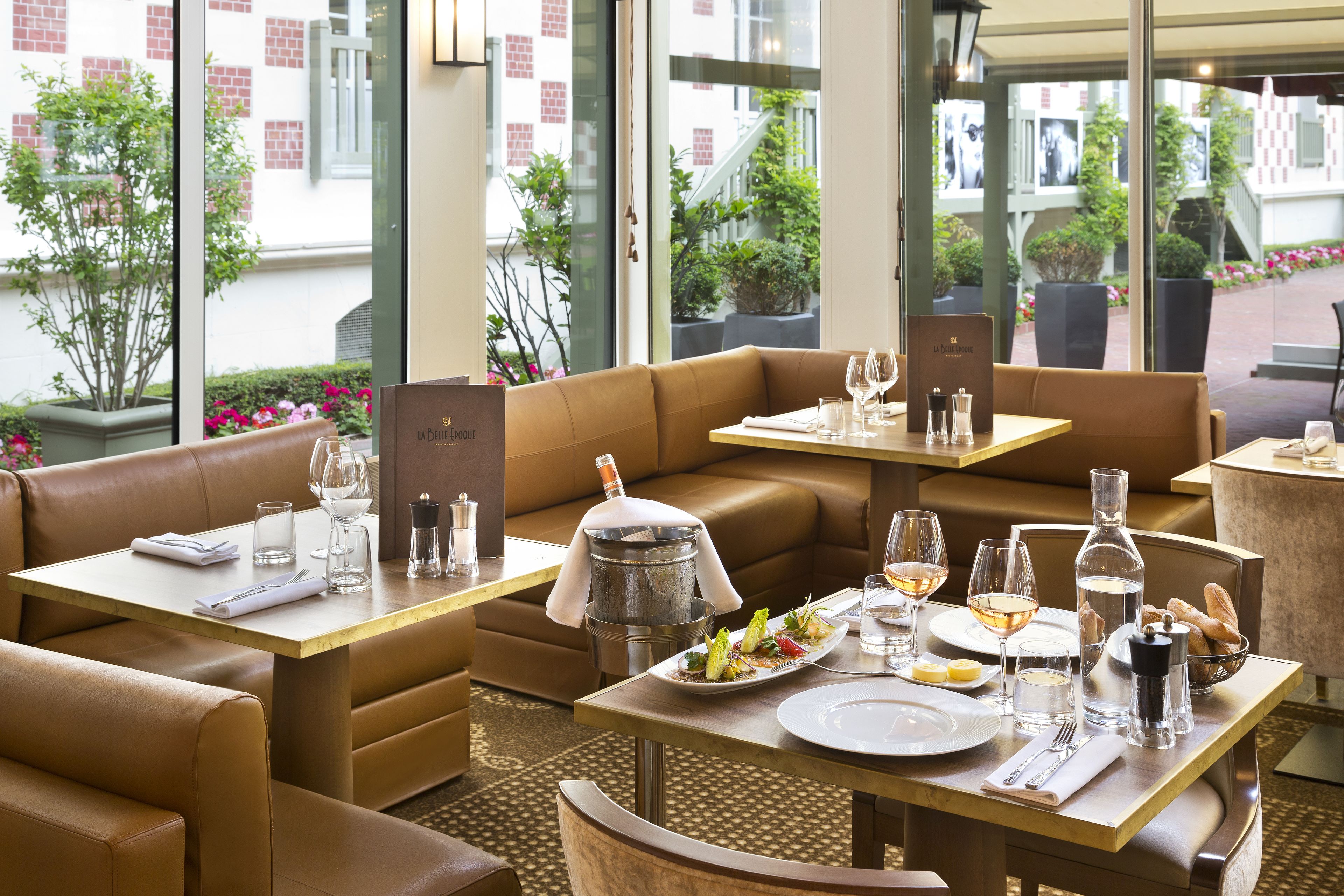 A restaurant with leather booths, tables set for dining, and a view of the street outside.