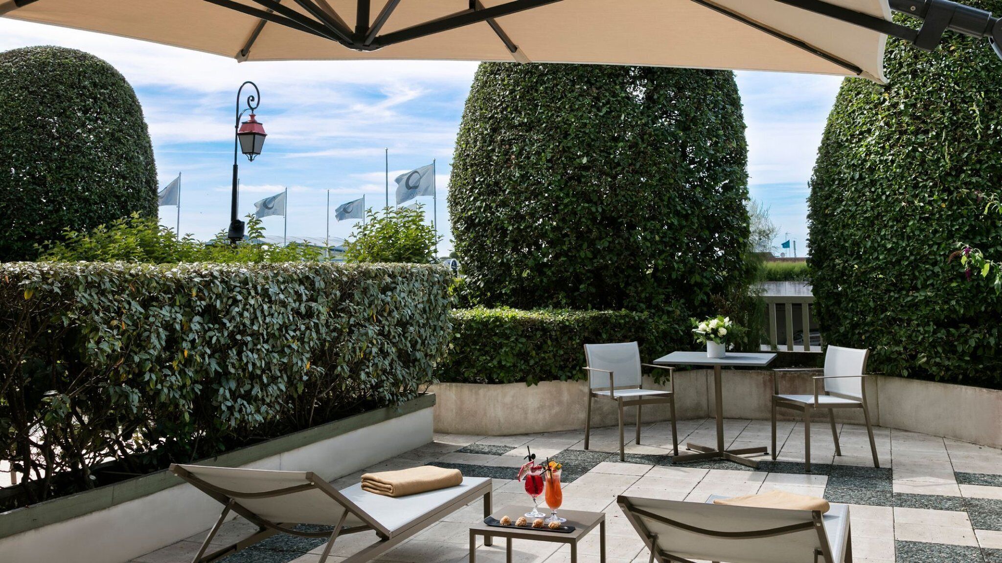 Un espace extérieur aménagé avec une table et des chaises, une petite table servant de bar avec des boissons et des en-cas, et des haies soigneusement taillées.