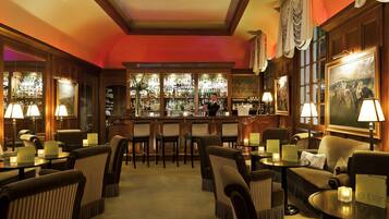 A bar area with multiple seating options, including bar stools and cushioned chairs, with a bar counter and shelves stocked with bottles.