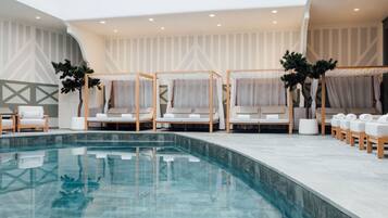 A modern indoor pool area with lounge chairs and a clear pool.