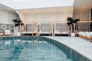 A modern indoor pool area with lounge chairs and a clear pool.