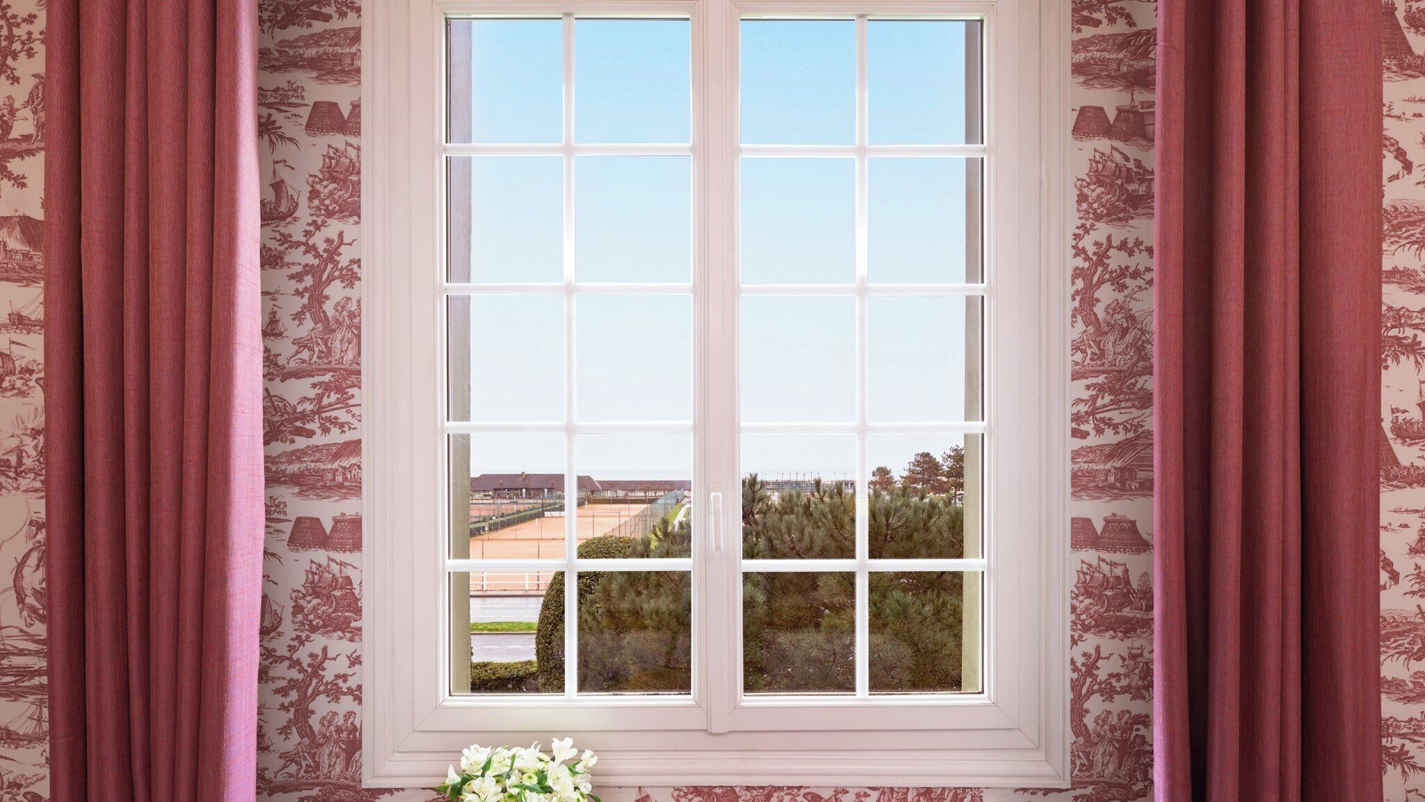 Ein Fenster mit Blick auf einen Tennisplatz und Bäume.