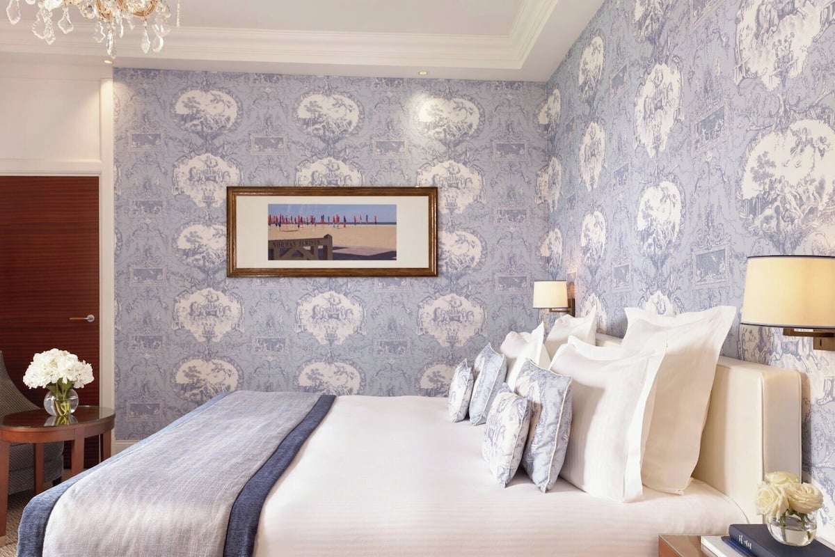 A hotel room with a large bed, a chair, a small table with a vase, and a framed picture on the wall.