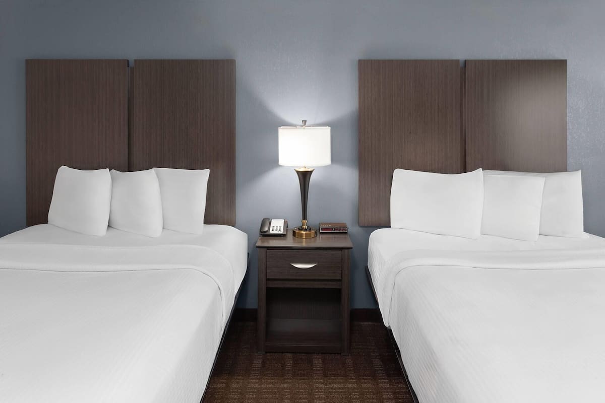 A hotel room with two beds, a nightstand with a lamp, a phone, and a small table.