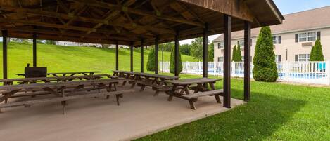 A covered picnic area with multiple wooden picnic tables and a concrete floor.