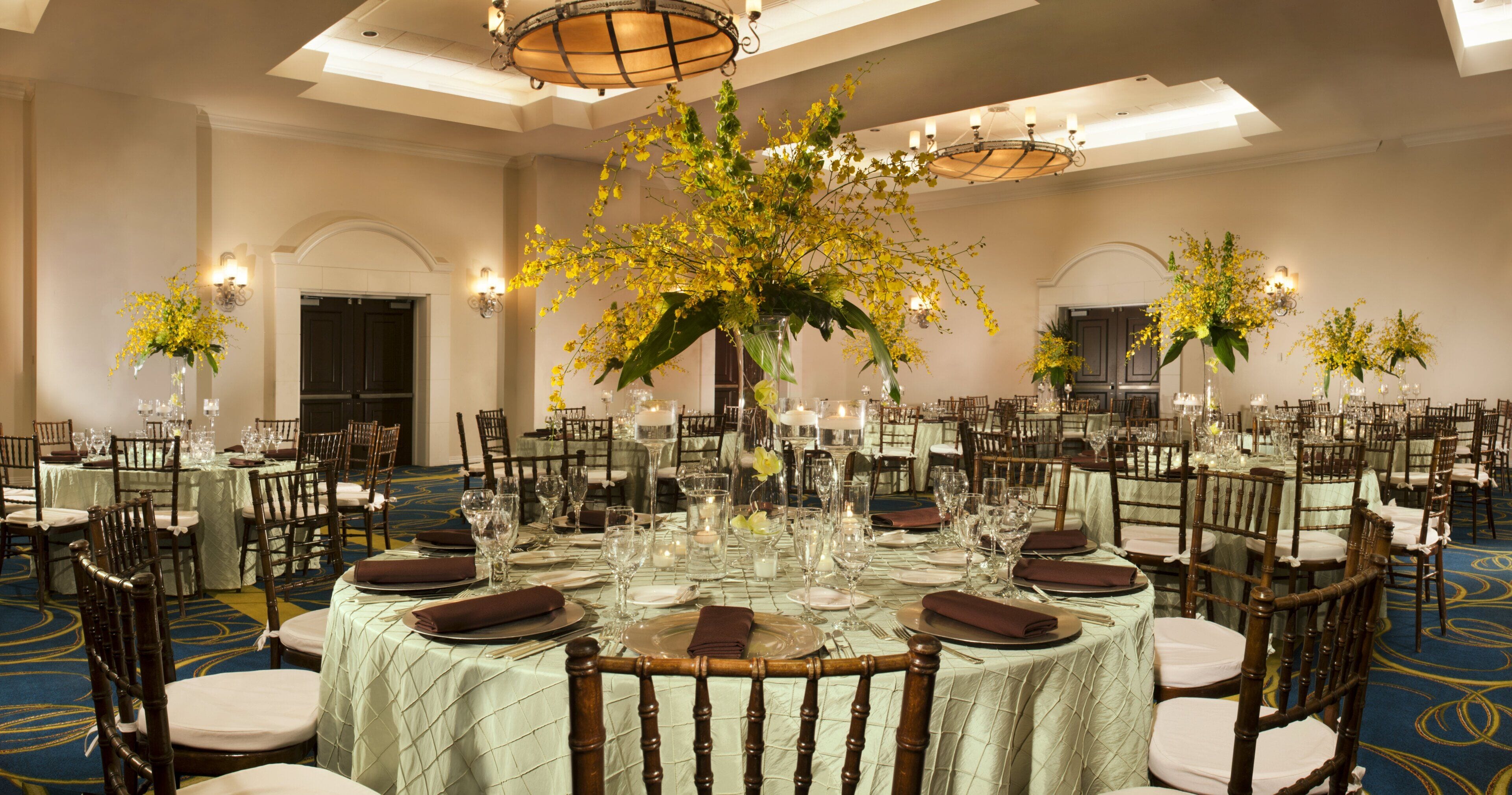 A banquet hall with round tables set for dining, featuring floral centerpieces and candlelight.