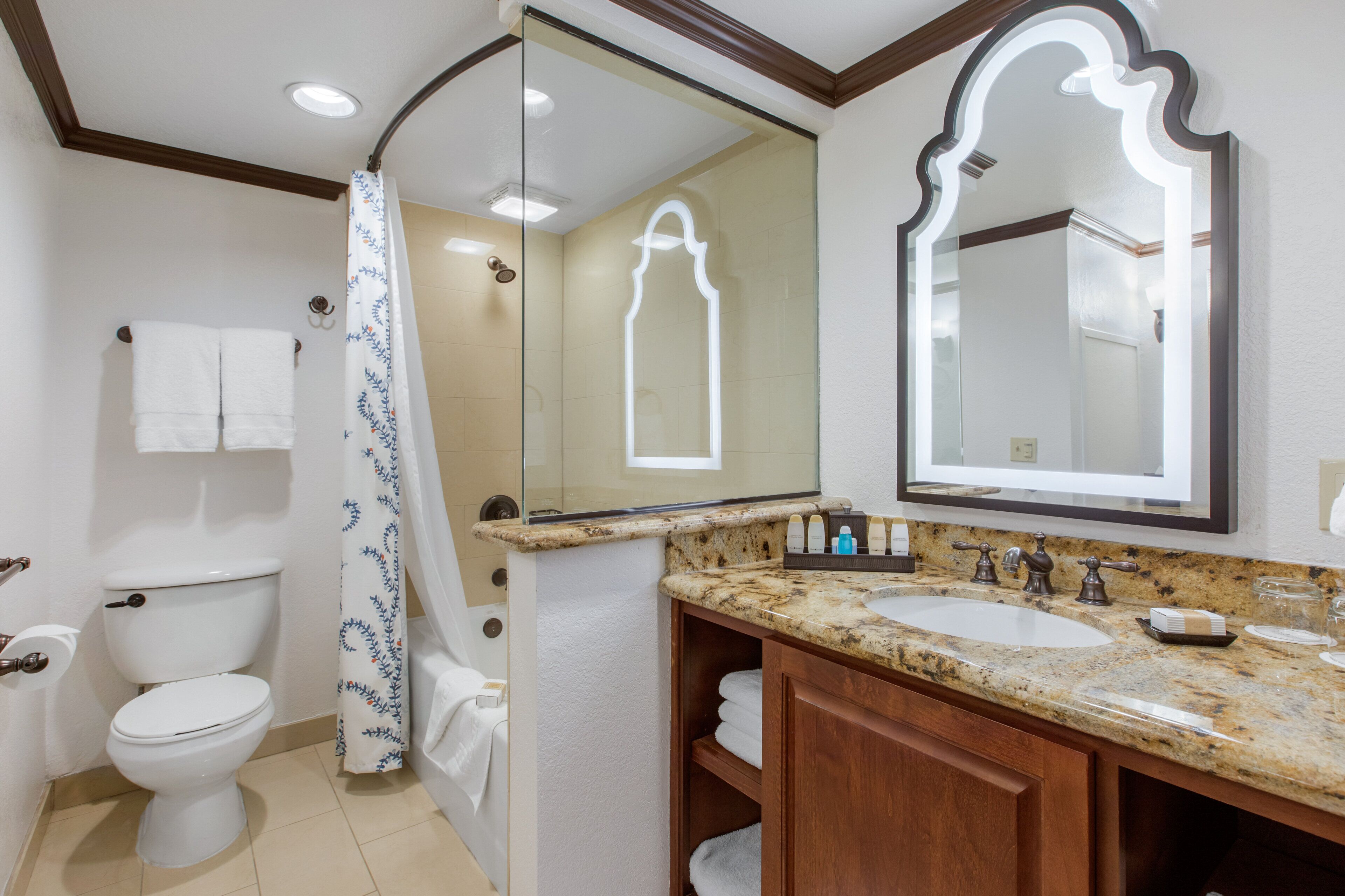 A bathroom with a toilet, shower, sink, and mirror.