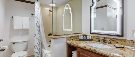 A bathroom with a toilet, shower, sink, and mirror.