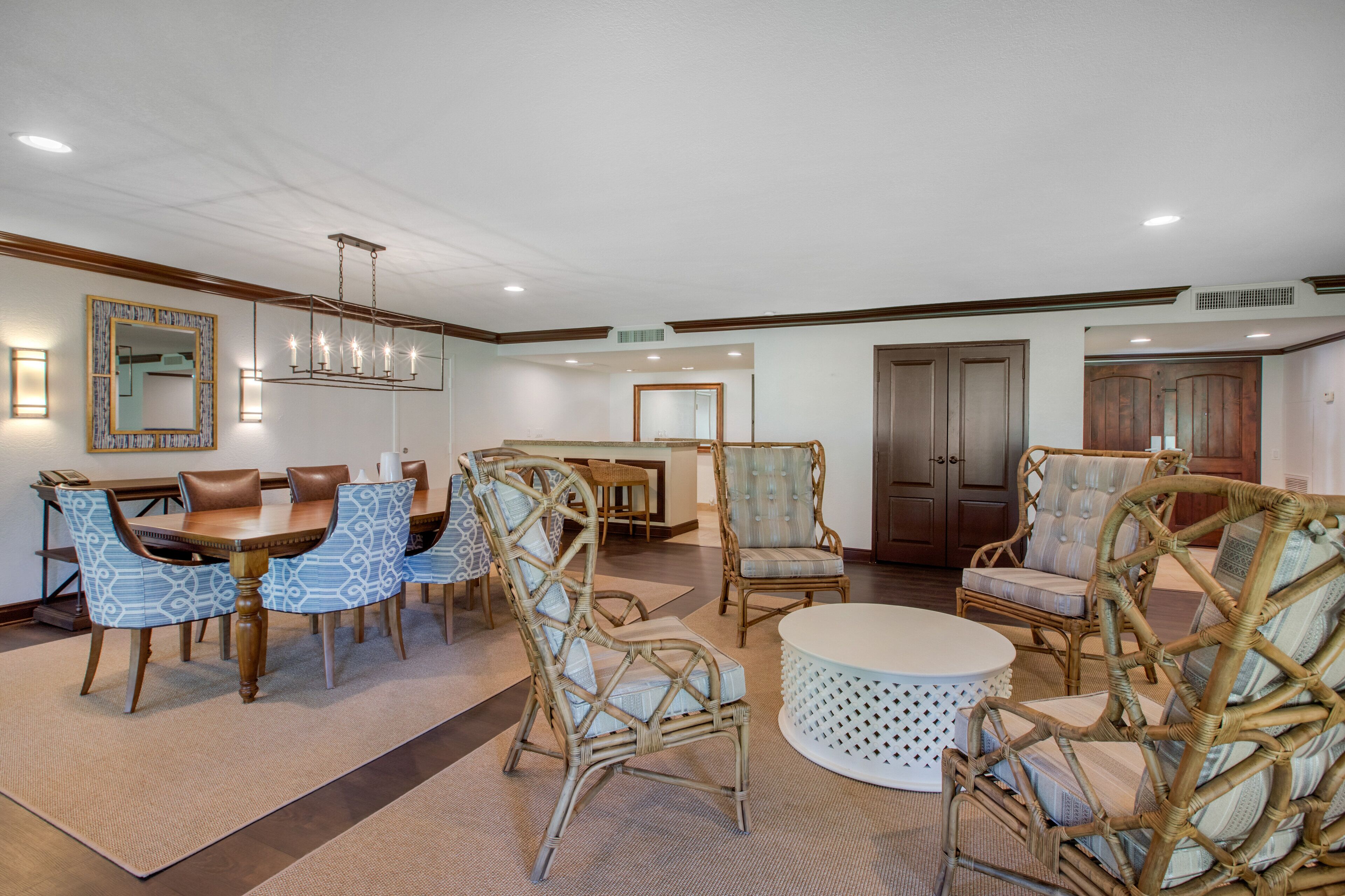 A spacious living room with a dining area, featuring wicker furniture, a round coffee table, and a chandelier.