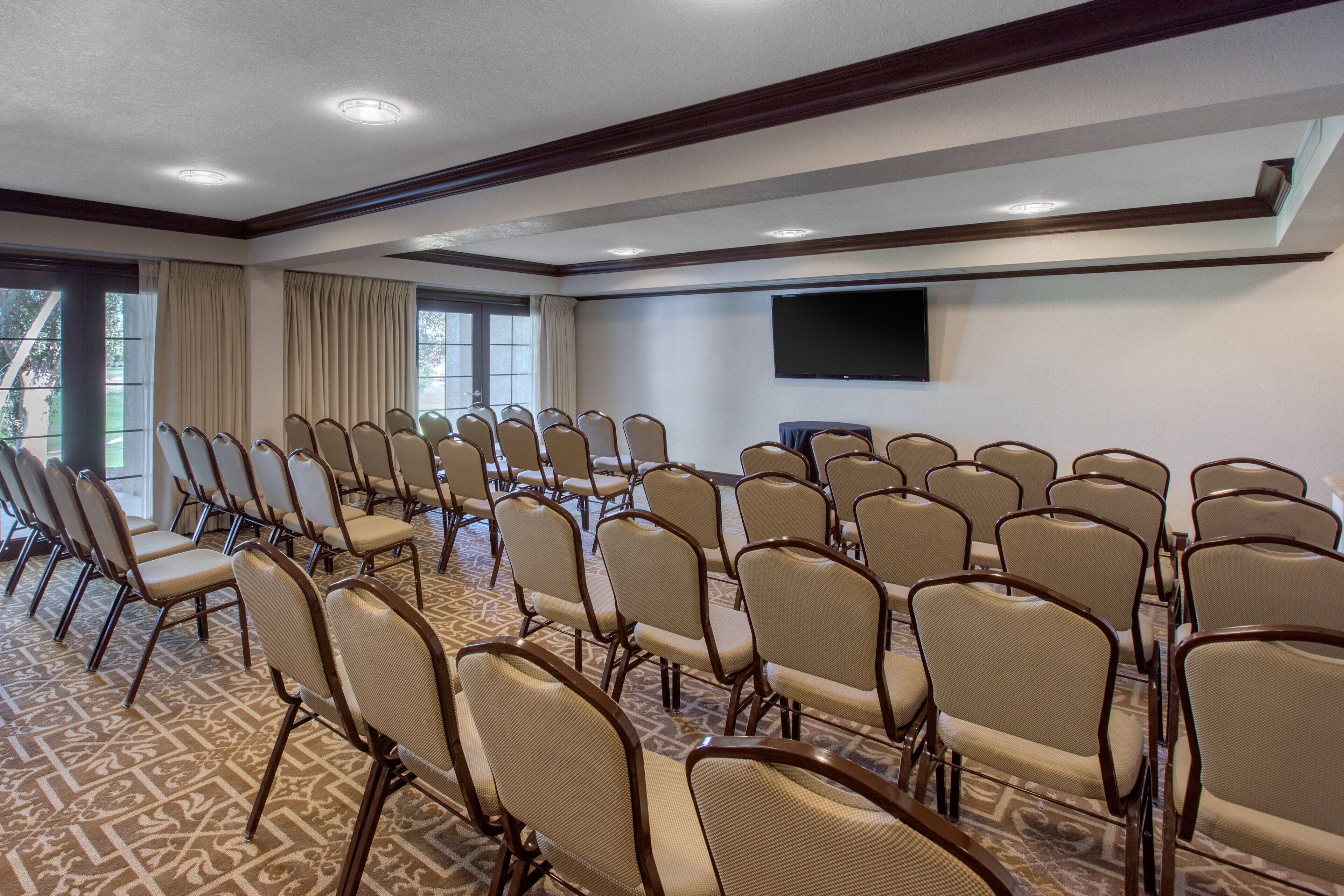 Une salle de conférence avec des rangées de chaises, un grand téléviseur à écran plat et une moquette à motifs.