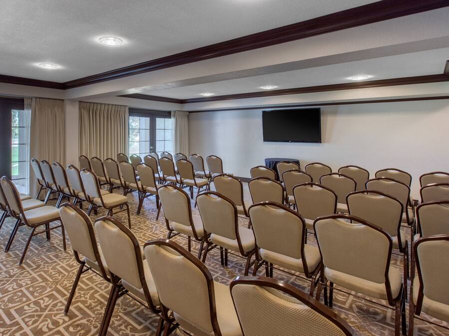 Un salón de conferencias con filas de sillas, un televisor de pantalla plana grande y alfombra estampada.