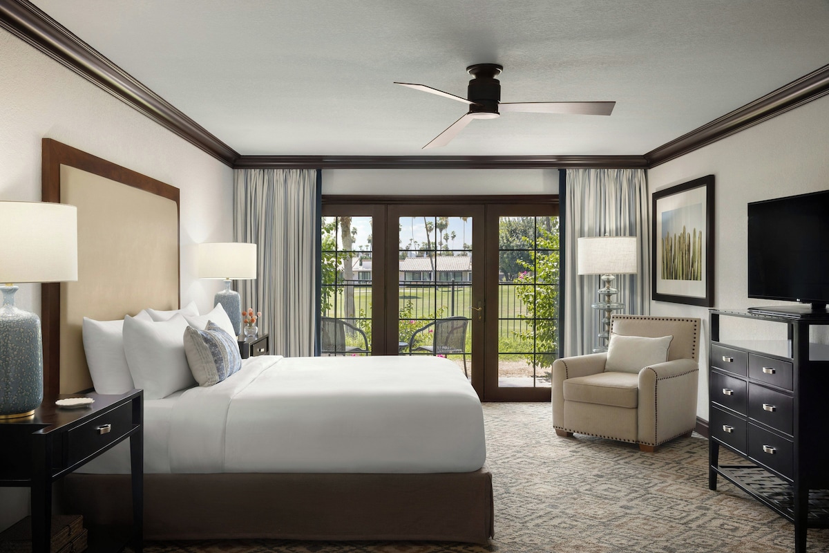 A hotel room with a bed, a desk, a chair, a dresser, and a television.