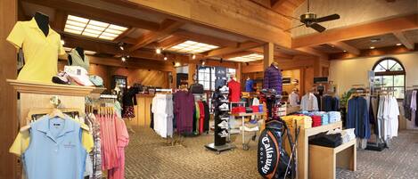 A clothing store with racks of shirts and pants, a golf bag display, and a ceiling fan.