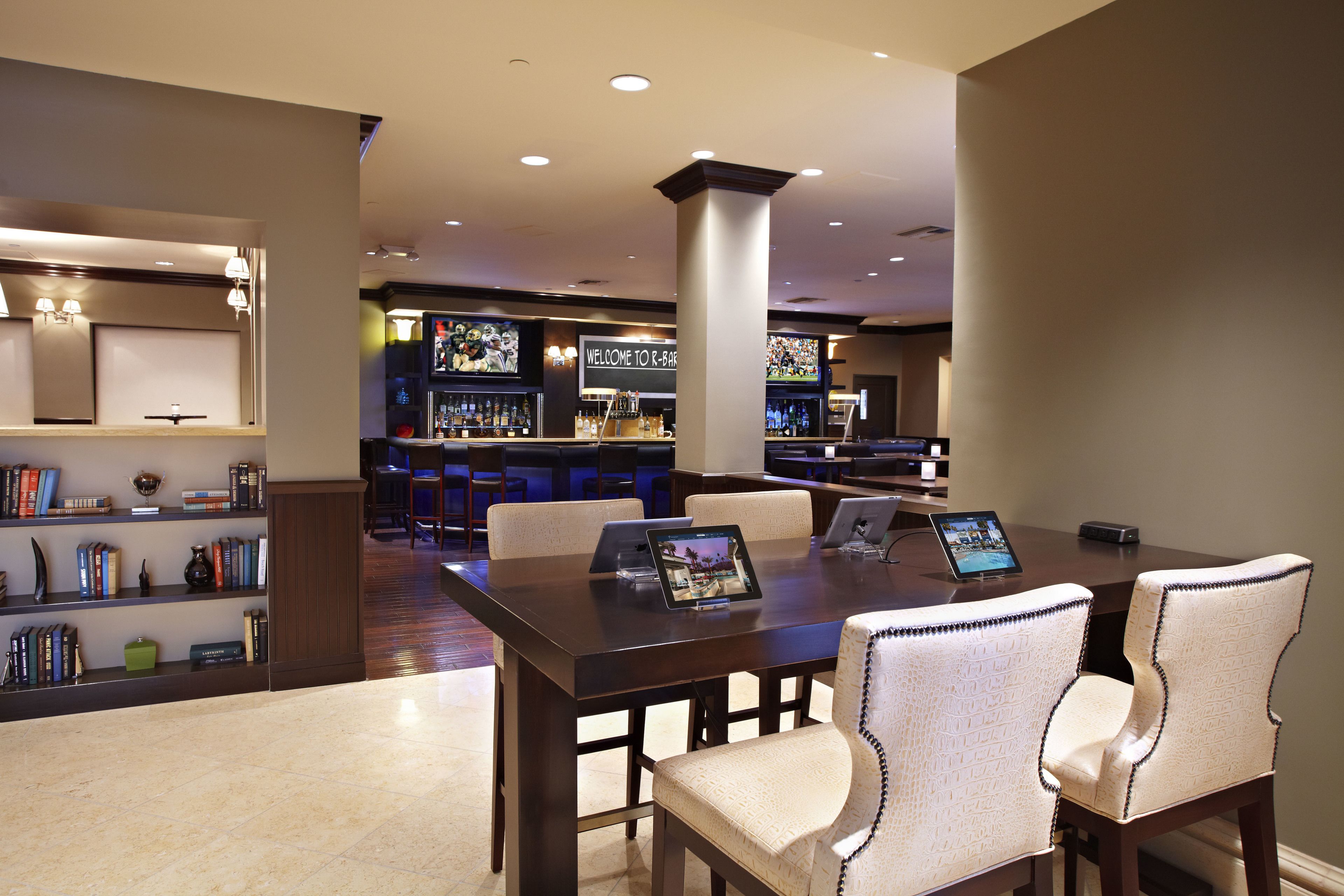 Eine moderne Hotelhalle mit Barbereich, einer Rezeption und einem Essbereich mit großem Tisch und Stühlen.