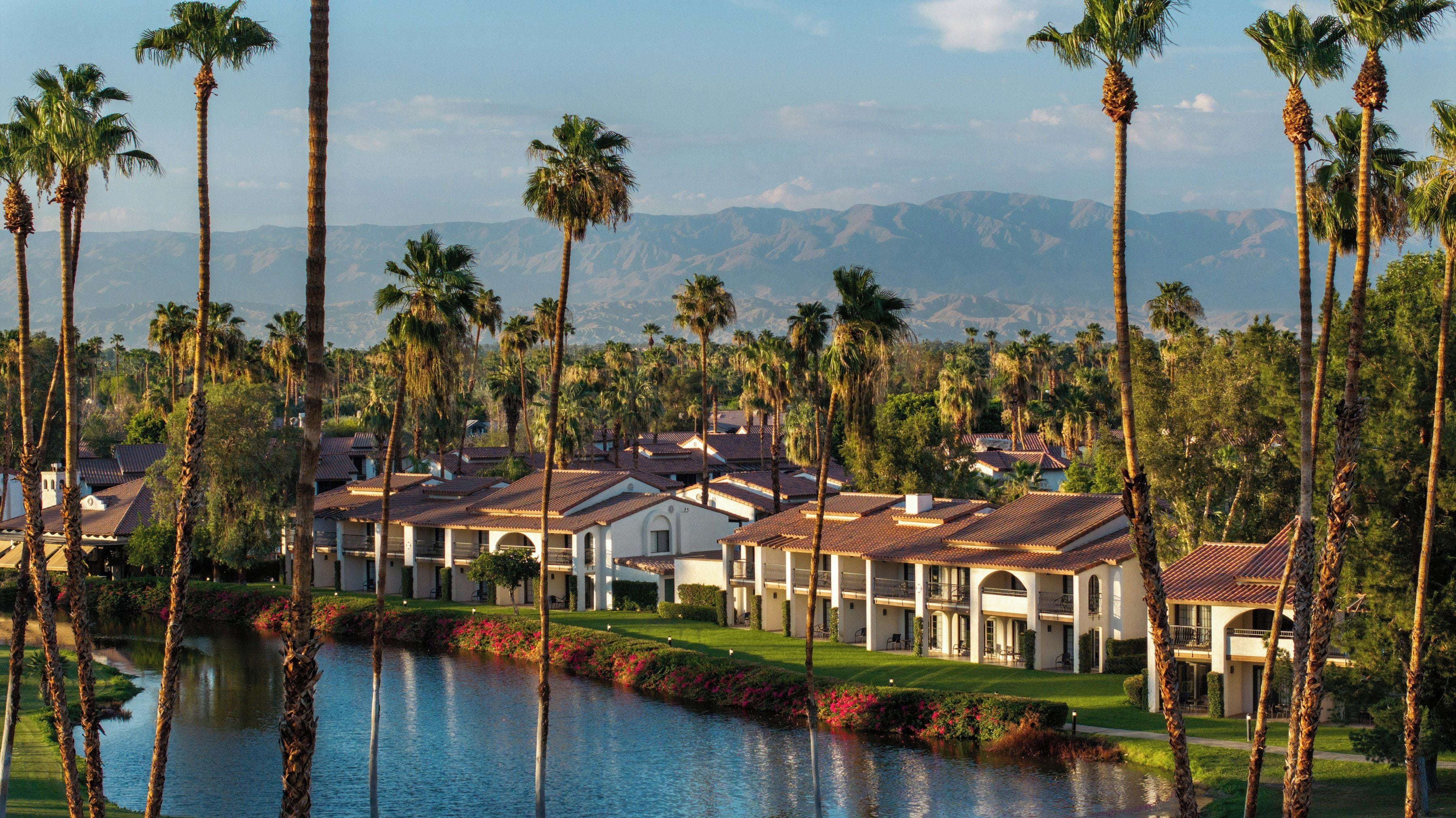 A resort with multiple-story buildings, a swimming pool, and palm trees.