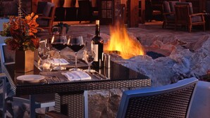 An outdoor seating area with a fire pit, tables, and chairs, and a bar visible through the open doorway. - Omni Rancho Las Palmas Resort & Spa (Rancho Mirage)