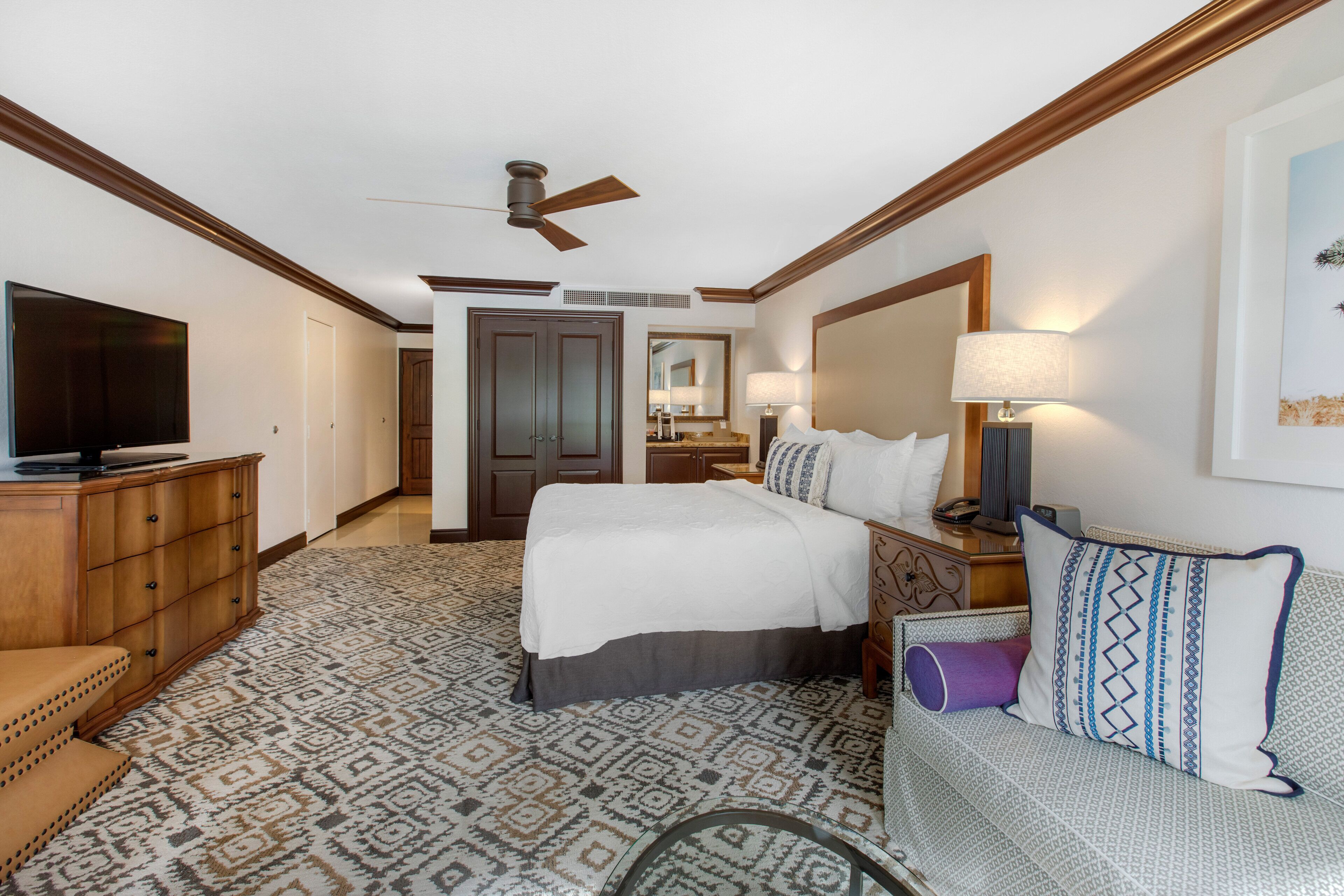 A hotel room with a bed, a TV, a desk, a chair, and a sofa.