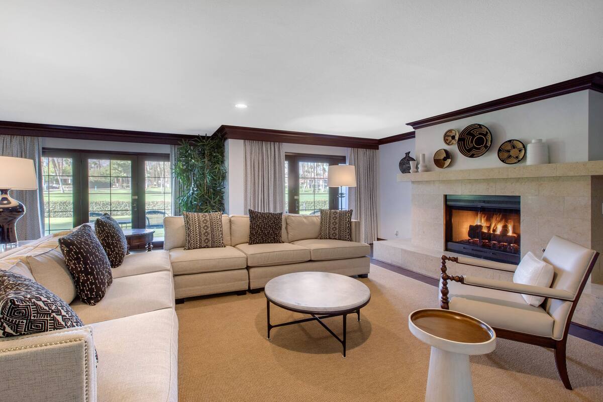 Un amplio salón con un sofá seccional color beige, una mesa de centro redonda y una chimenea.