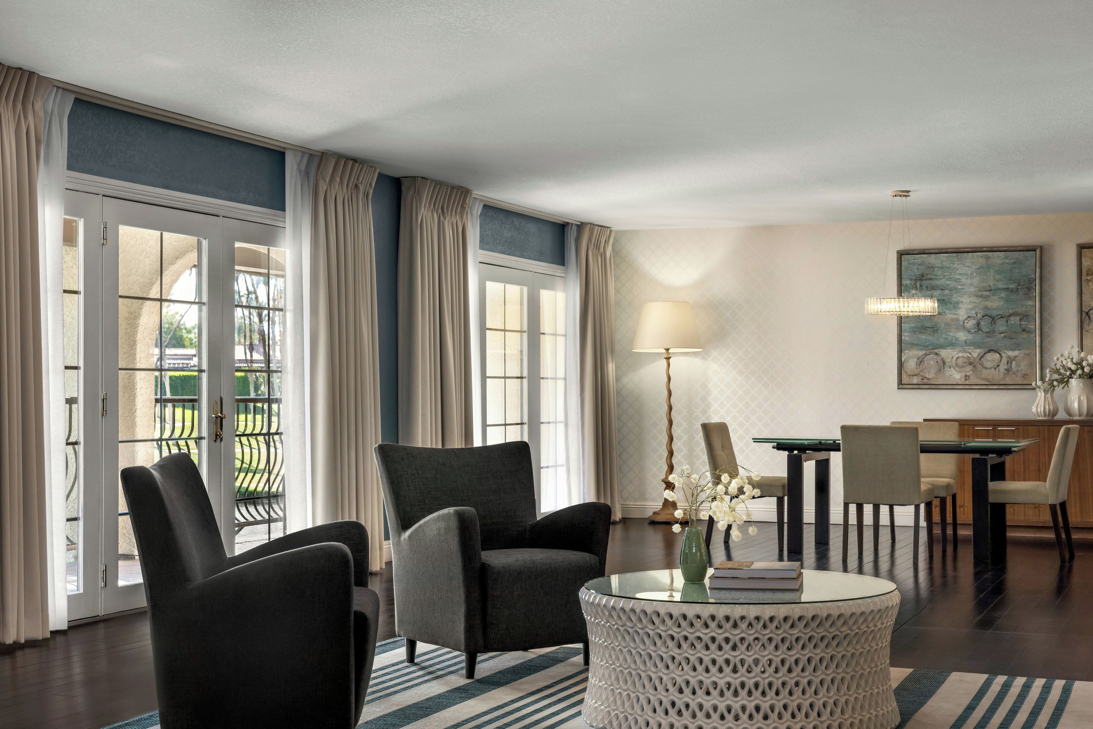 Habitación de hotel con zona de estar, mesa de comedor y vistas a través de puertas de cristal.