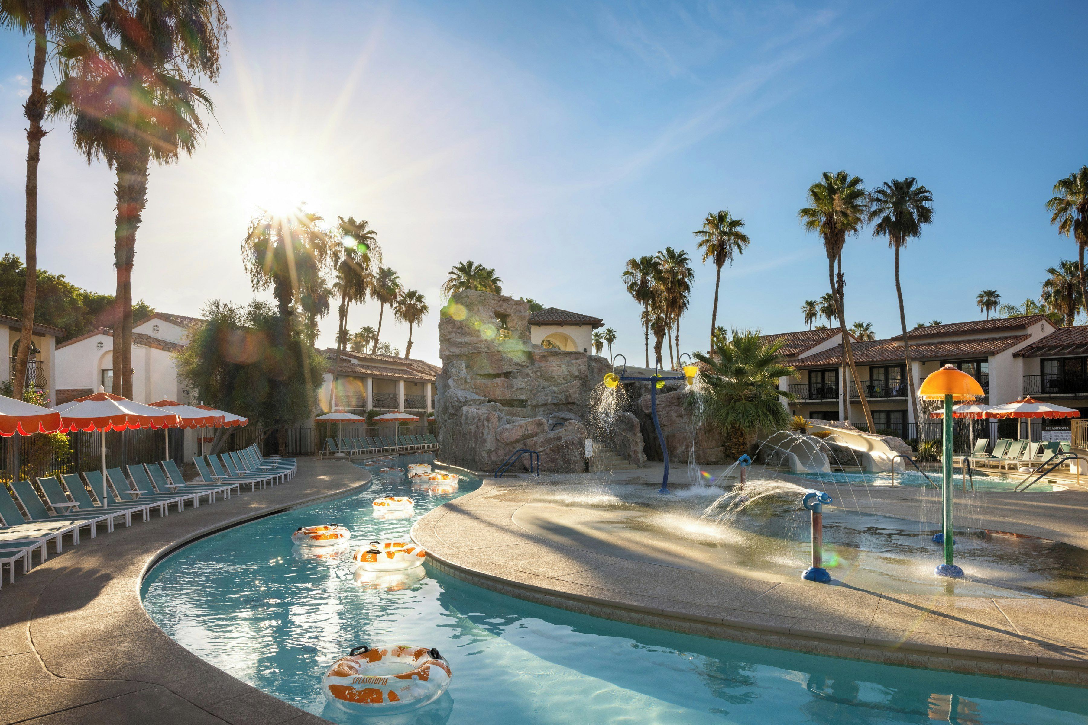 A pool area with lounge chairs, a water feature, and palm trees.