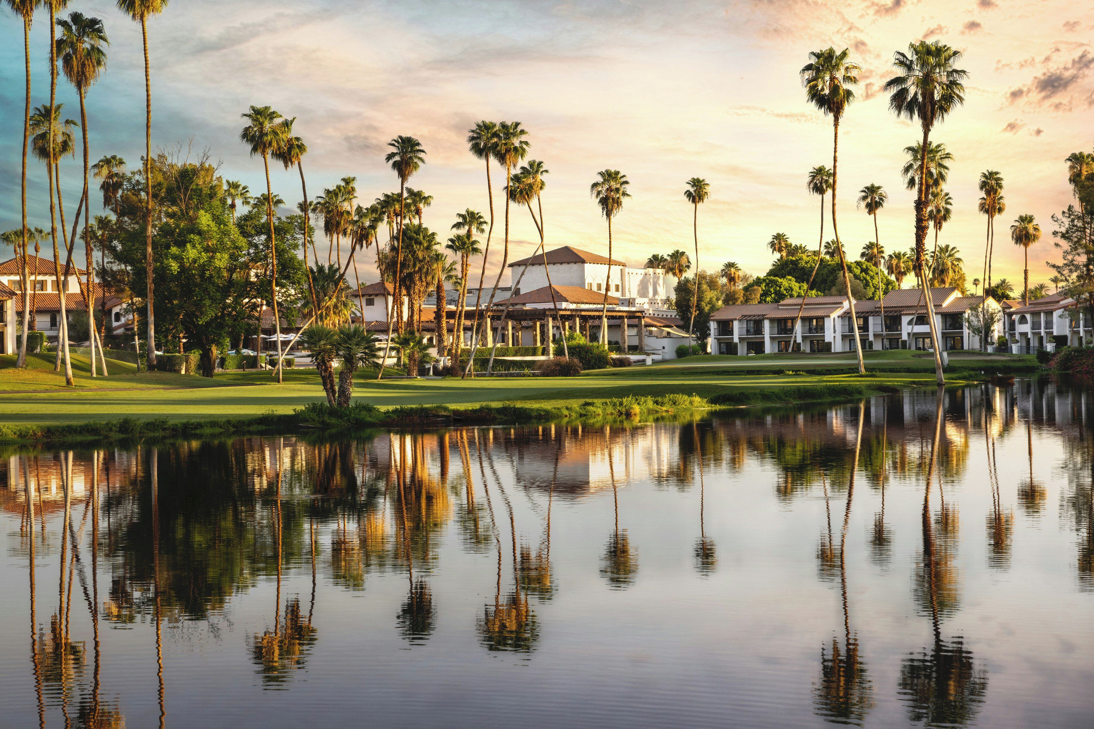 A resort with multiple buildings, a golf course, and a calm lake reflecting the surroundings.
