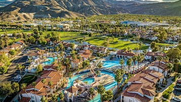 Un resort con varias piscinas, palmeras y montañas al fondo.