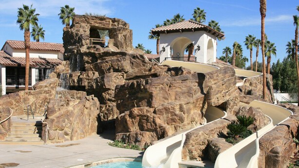 A pool area with a rock formation, a water slide, and a building with a tiled roof. - Omni Rancho Las Palmas Resort & Spa (Rancho Mirage)
