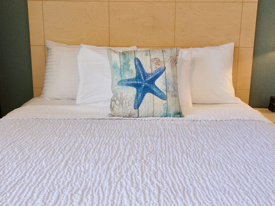 Une chambre d’hôtel avec un lit agrémenté d’une couverture blanche à motifs, d’une tête de lit en bois et d’un coussin décoratif orné d’un motif d’étoile de mer.
