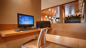 A reception desk with a computer, keyboard, and mouse. There is a chair in front of the desk. The room has wooden paneling and a tiled floor.