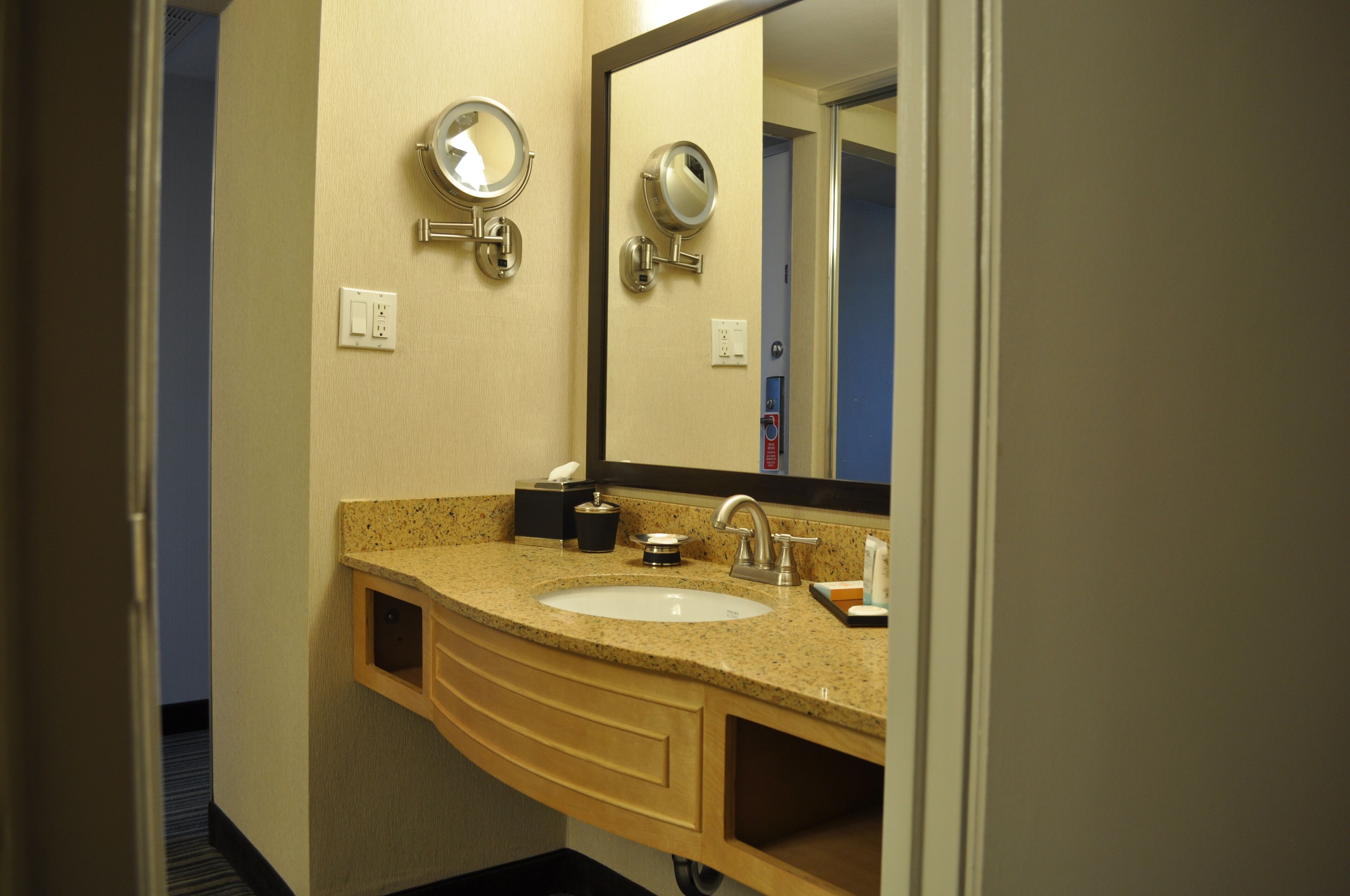 A bathroom with a sink, mirror, and towel dispenser.