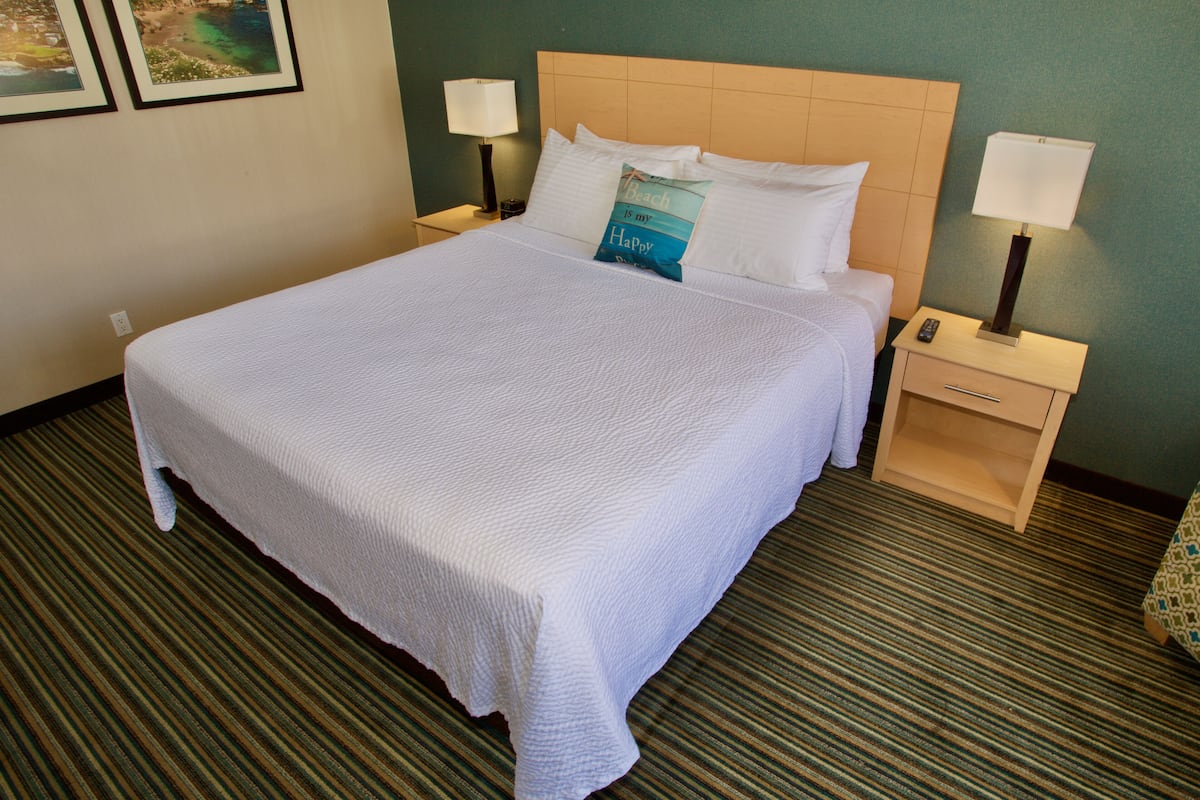 Une chambre d’hôtel avec un grand lit, deux tables de chevet, une petite table et une tête de lit.