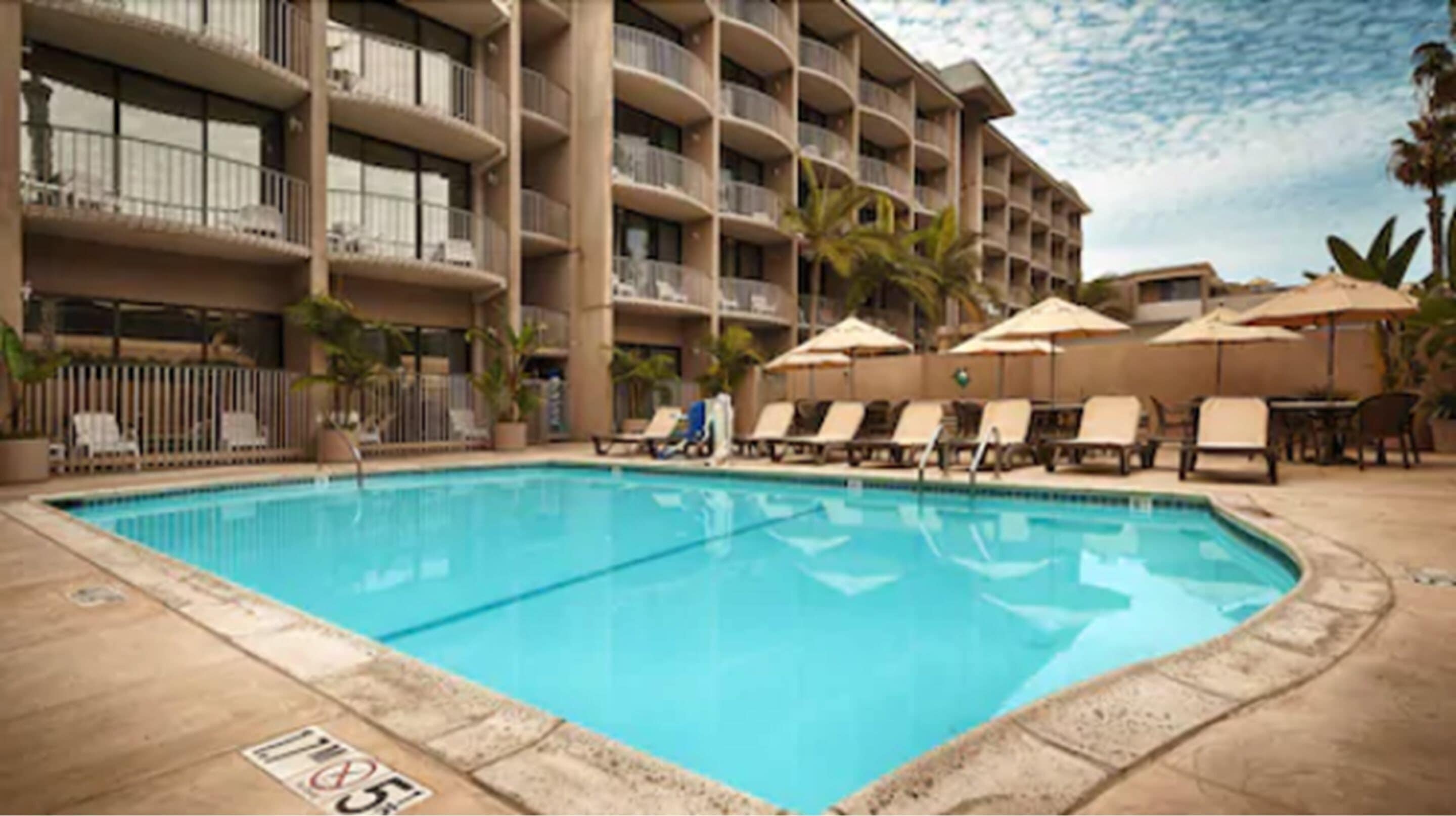 A hotel pool area with a clear blue pool, sun loungers, and umbrellas.