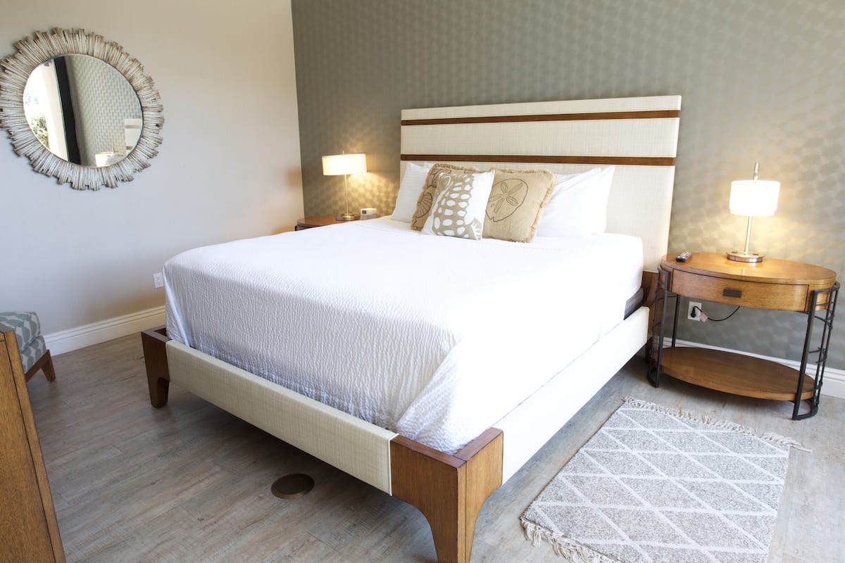 Une chambre à coucher bien aménagée, avec un grand lit, deux tables de chevet avec des lampes, un grand miroir rond et un tapis à motifs.
