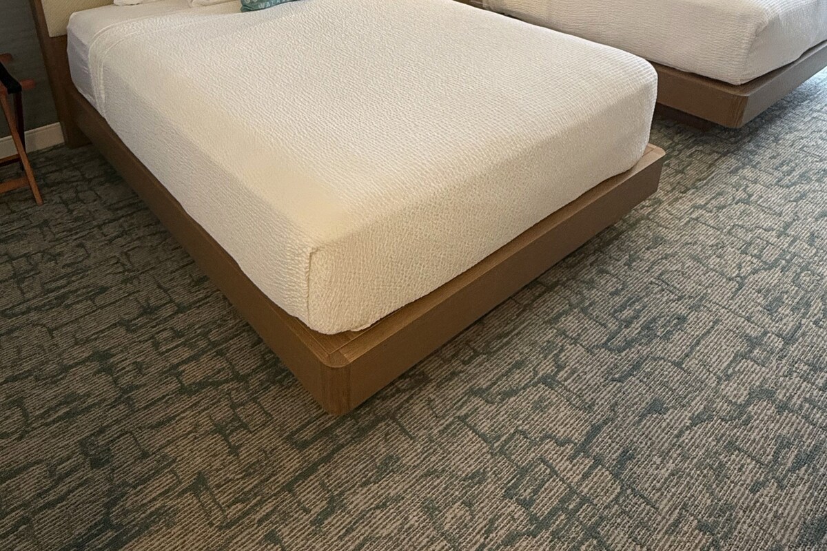A hotel room with two beds, a nightstand, a lamp, and a window with curtains.