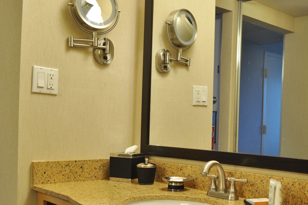 A bathroom with a granite countertop, a sink, a mirror, and a door in the background.