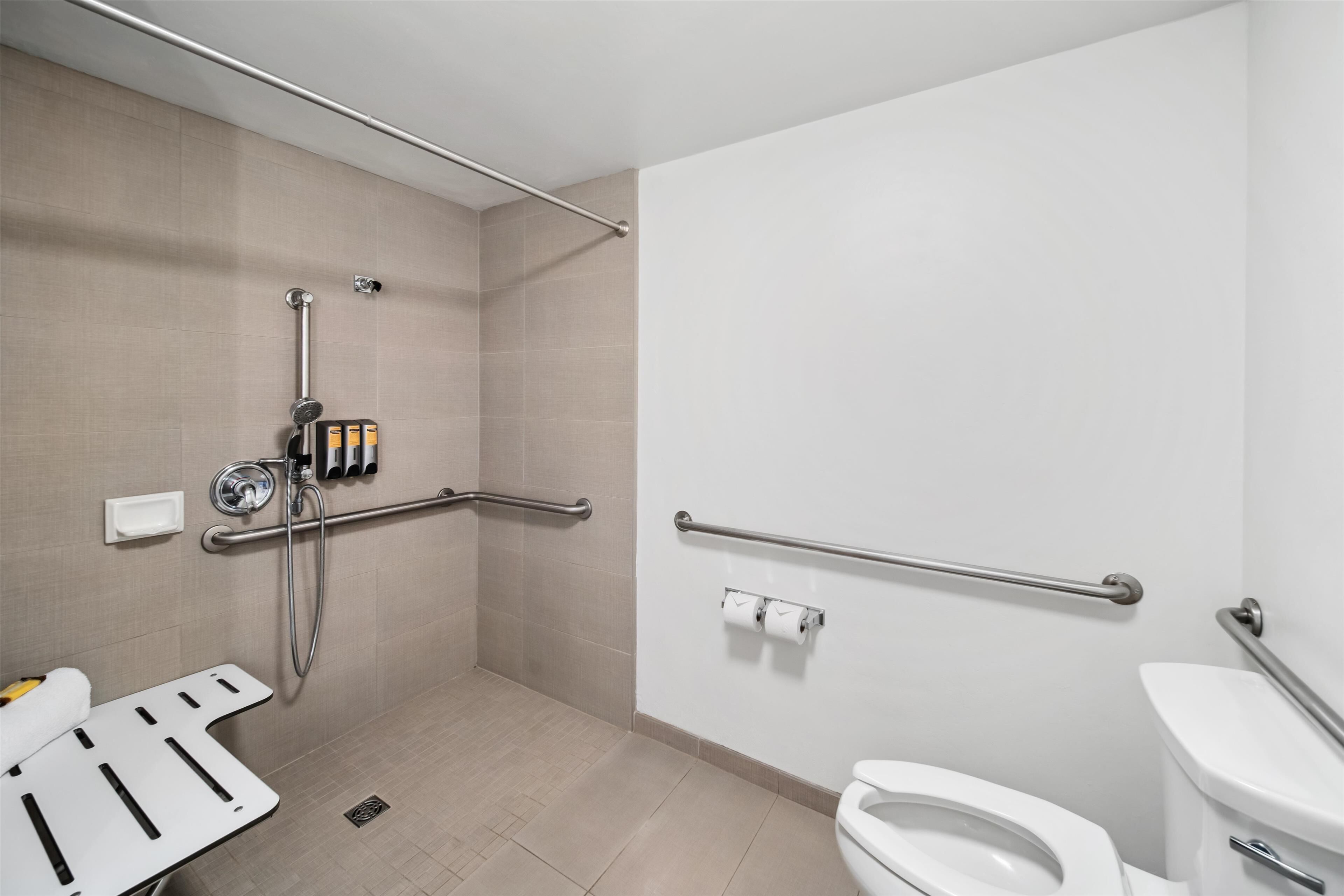 A bathroom with a shower, toilet, and grab bars.