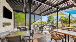 An outdoor cafe with tables and chairs, a brick wall, and a large window with blinds. - Best Western Plus Hilltop Inn (Redding)