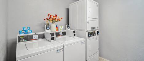 Un espace buanderie équipé d’un lave-linge et d’un sèche-linge à chargement frontal, d’une petite étagère avec des articles de toilette et d’un vase avec des fleurs.