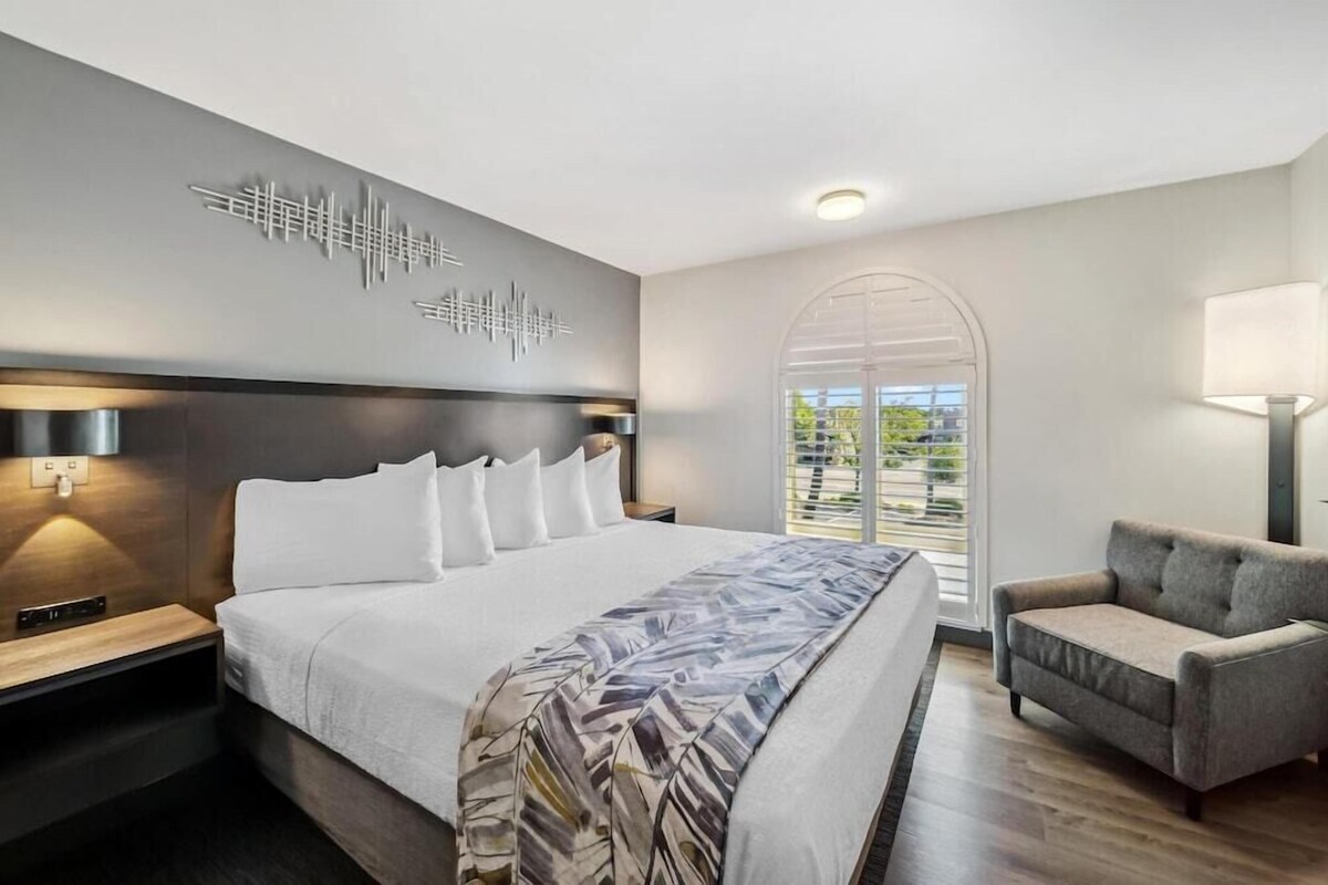 Camera d'albergo moderna con un letto grande, un divano, un'opera d'arte a parete e vista su spazi verdi.