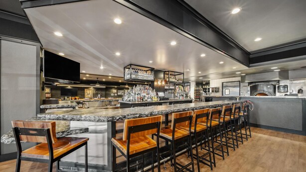 A modern bar area with a long counter, multiple stools, and a large screen. - Best Western Plus Hilltop Inn (Redding)
