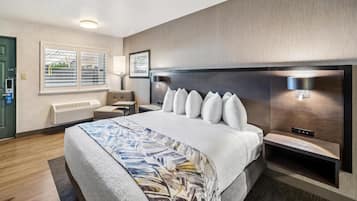 A modern hotel room with a large bed, a desk, a chair, and a window with blinds.